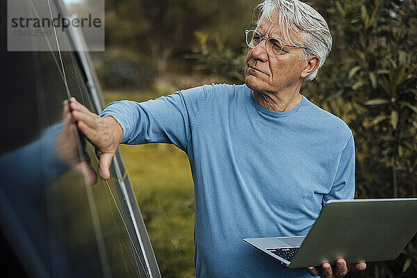 Älterer Mann mit Laptop  der Sonnenkollektoren berührt