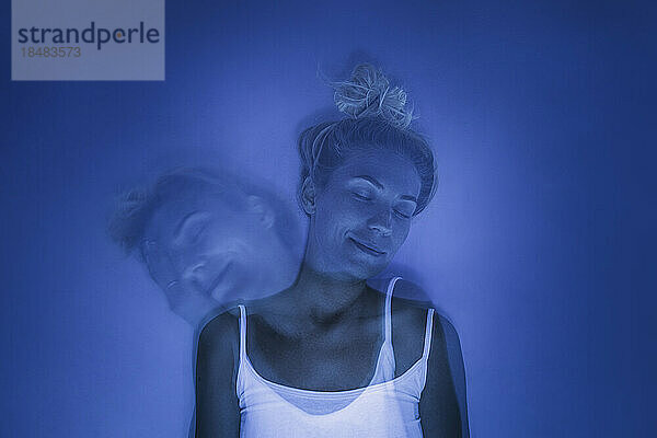 Lächelnde Frau mit geschlossenen Augen unter UV-Licht vor blauem Hintergrund