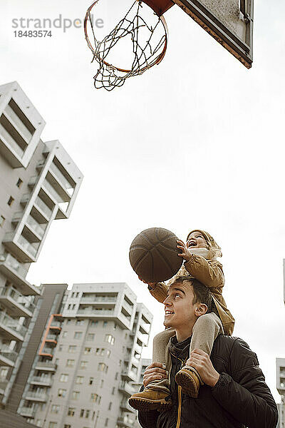 Vater trägt Tochter auf Schultern und spielt Basketball