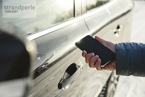 Hand eines Mannes  der sein Smartphone im Auto benutzt