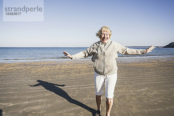 Glückliche  unbeschwerte ältere Frau mit ausgestreckten Armen  die am Strand tanzt