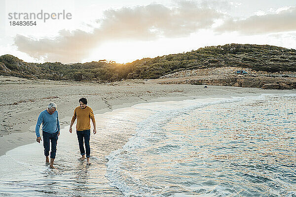 Mann geht mit Vater bei Sonnenuntergang am Strand spazieren