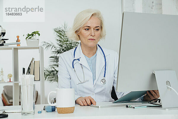 Älterer Arzt  der am Schreibtisch am Desktop-PC arbeitet
