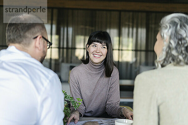 Lächelnde Frau bei einem Treffen mit Geschäftsmann und Geschäftsfrau im Büro