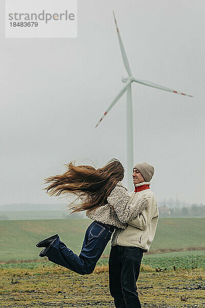 Glücklicher Teenager-Freund dreht Freundin vor Windkraftanlage