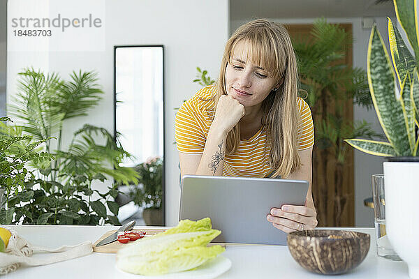 Frau mit Hand am Kinn schaut sich Tutorial über Tablet-PC an