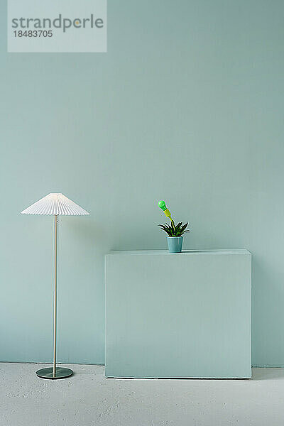 Stehlampe mit Glühbirne auf Zimmerpflanze vor blauer Wand