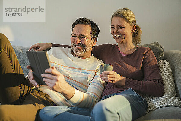 Glückliches älteres Paar schaut sich zu Hause auf dem Sofa einen Tablet-PC an