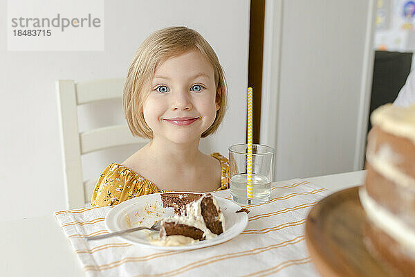 Lächelndes Mädchen  das mit Kuchen am Tisch sitzt