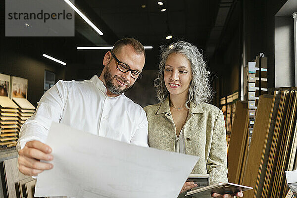 Two confident colleagues holding plan in architect's office