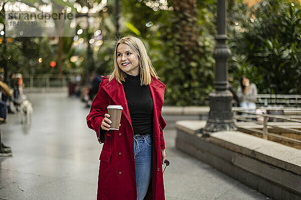 Lächelnde reife Frau hält Einwegkaffeetasse auf Fußweg