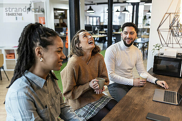 Geschäftsfrau lacht mit Kollegen in der Kaffeepause im Büro