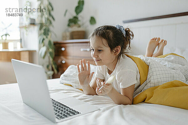 Lächelndes Mädchen winkt zu Hause per Videoanruf über den Laptop