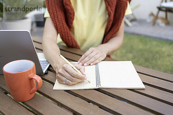 Hände eines Freiberuflers schreiben Notizen auf dem Tisch im Garten