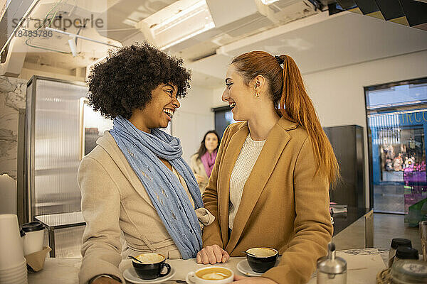 Fröhliche junge Frau lacht mit einer Freundin  die im Café steht