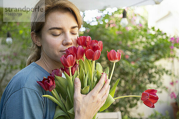 Frau mit geschlossenen Augen riecht einen Strauß Tulpenblüten