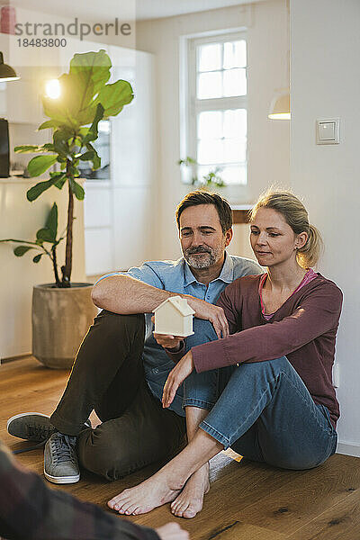 Mann und Frau mit Hausmodell sitzen zu Hause auf dem Boden