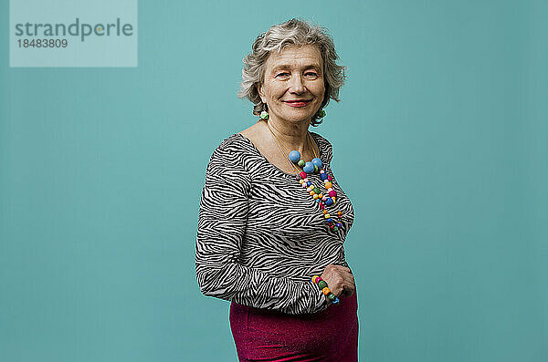 Lächelnde ältere Frau mit buntem Schmuck vor türkisfarbenem Hintergrund
