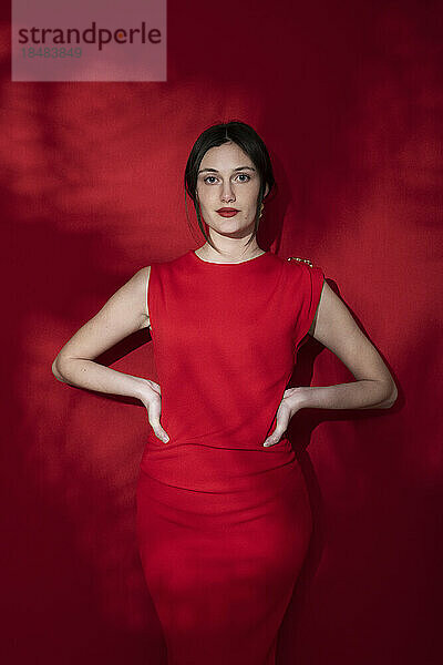 Selbstbewusste Frau mit den Händen auf den Hüften vor rotem Hintergrund