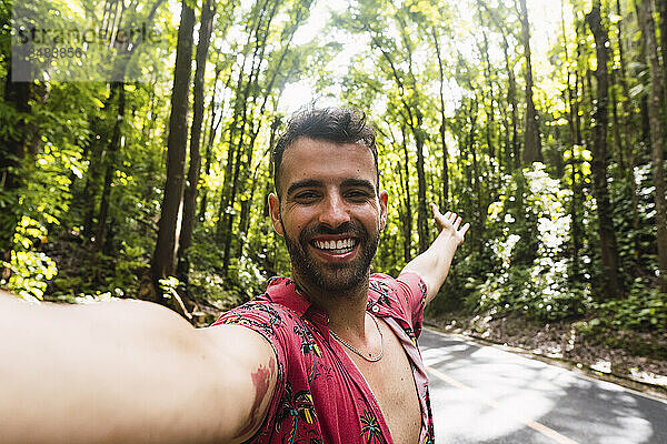 Fröhlicher Mann macht ein Selfie auf der Straße vor Bäumen