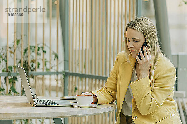 Blonde Geschäftsfrau spricht im Café mit Smartphone