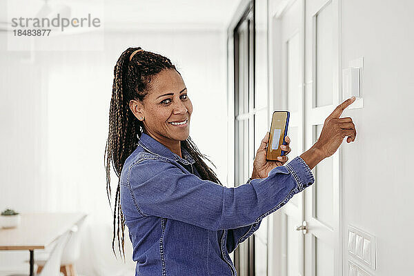 Glückliche reife Frau  die den Thermostat über die Smartphone-App einstellt