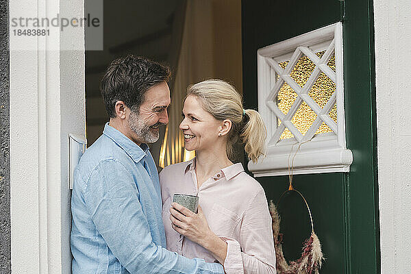Glücklicher reifer Mann umarmt seine Frau mit einer Tasse am Eingang des Hauses