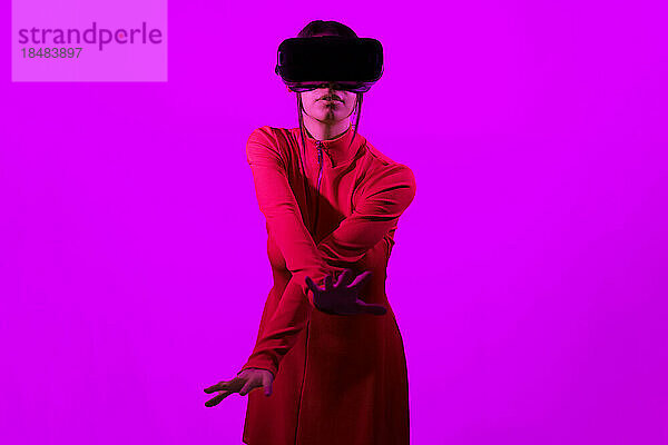 Junge Frau mit Virtual-Reality-Brille gestikuliert vor rosa Hintergrund