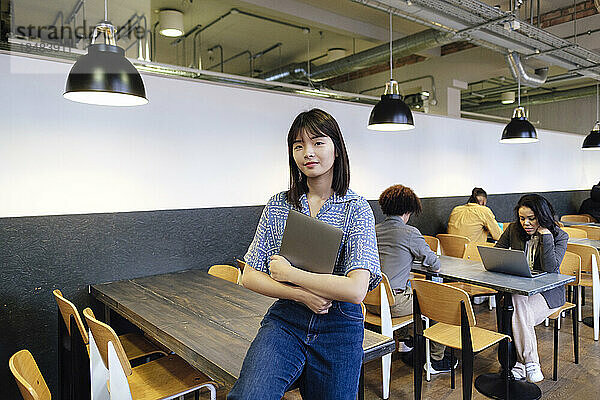 Junge Geschäftsfrau mit Laptop sitzt am Tisch im Büro