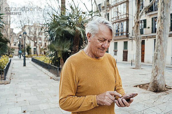 Älterer Mann benutzt Smartphone am Fußweg