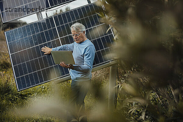 Älterer Mann benutzt Laptop und untersucht Sonnenkollektoren