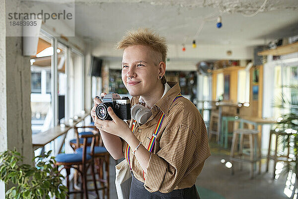 Lächelnde nicht-binäre Person mit Kamera beim Fotografieren im Café