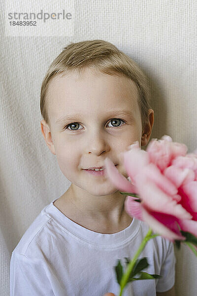 Netter Junge  der rosa Blume hält