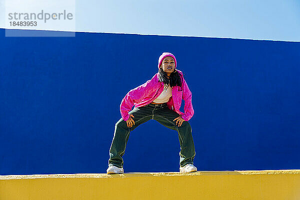 Selbstbewusster junger Tänzer in rosa Jacke tanzt an der Wand