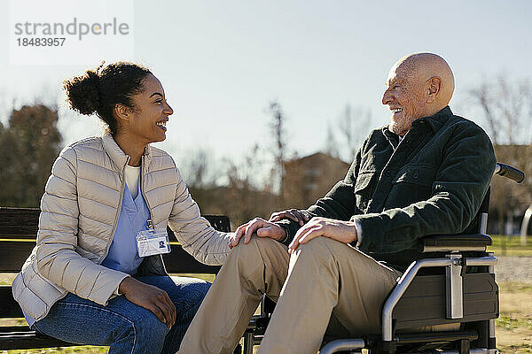 Glücklicher Hausmeister mit älterem Mann  der im Rollstuhl im Park sitzt