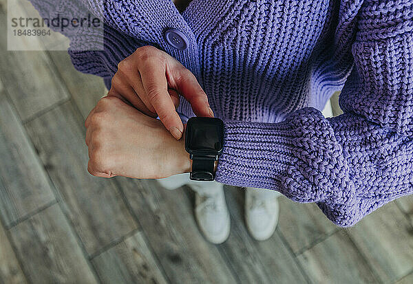Frau trägt einen lila Pullover und überprüft die Uhrzeit auf einer Smartwatch