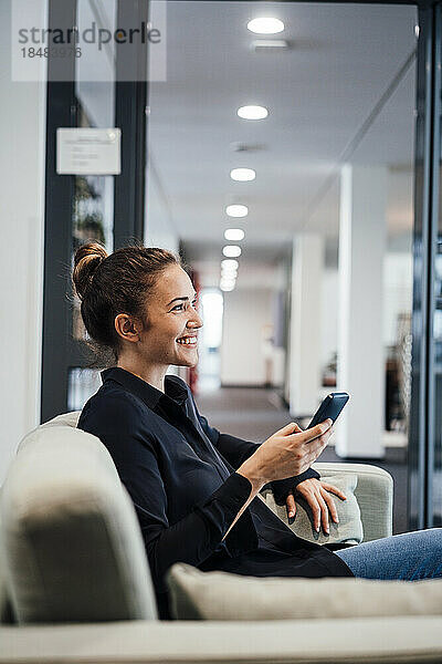 Glückliche Geschäftsfrau sitzt mit Mobiltelefon im Büro
