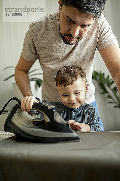 Netter Sohn hilft Vater beim Bügeln von Kleidung zu Hause