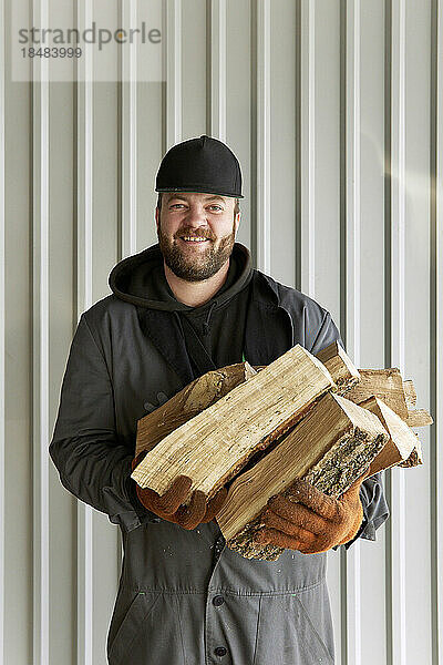 Lächelnder Koch mit Brennholz vor der Wand