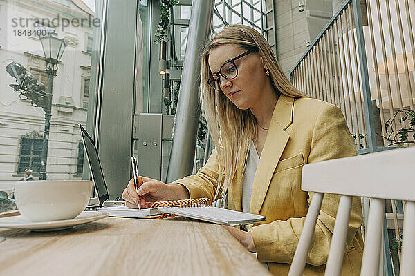 Geschäftsfrau schreibt Tagebuch und sitzt am Tisch im Café