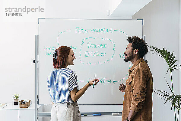 Lächelnde Geschäftsfrau diskutiert mit einem Kollegen  der vor dem Whiteboard steht