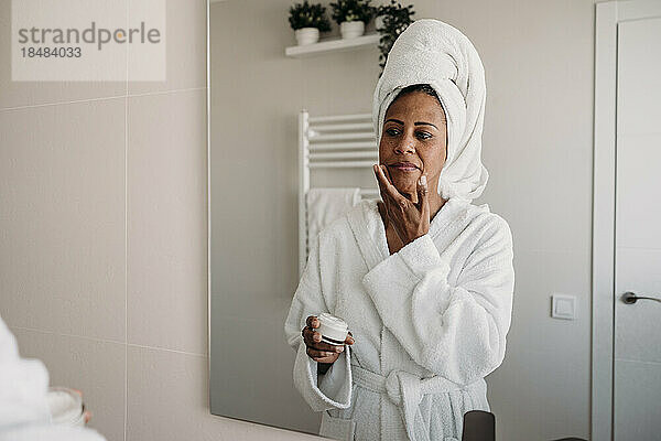 Reife Frau trägt im Badezimmer Feuchtigkeitscreme auf ihr Gesicht auf