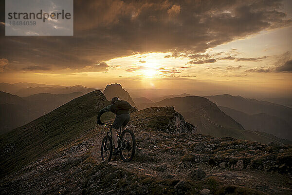 Mann fährt bei Sonnenuntergang mit dem Mountainbike auf dem Weg