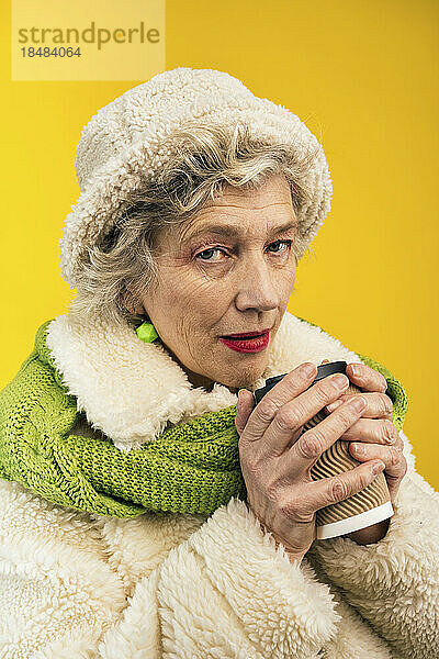 Ältere Frau mit Einwegkaffeetasse vor farbigem Hintergrund