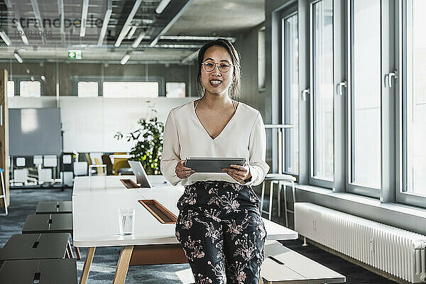 Lächelnde Geschäftsfrau hält Tablet-PC am Arbeitsplatz