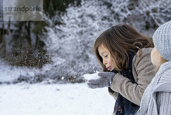 Nettes Mädchen  das von seiner Schwester Schnee auf die Hand bläst