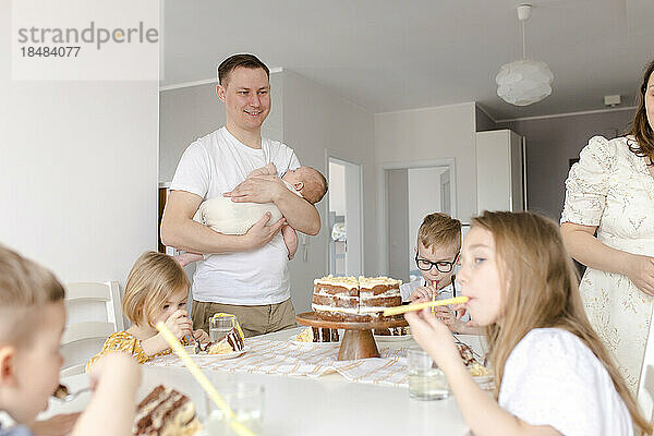Vater trägt Sohn mit Kindern  die am Tisch Kuchen essen