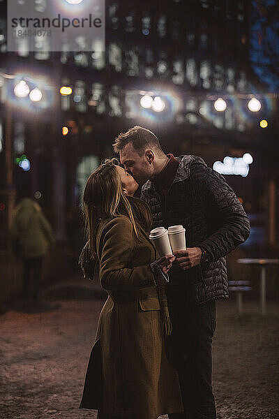 Romantic couple with disposable cups kissing each other at night
