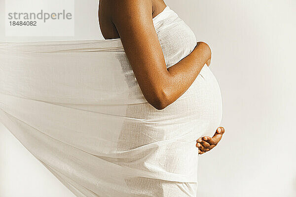Schwangere Frau mit weißem Laken bedeckt vor der Wand