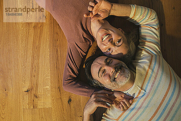 Smiling married couple lying on hardwood floor at home